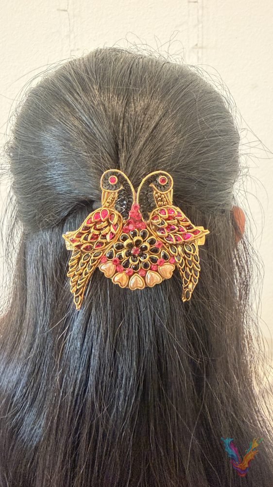 A gold and pink twin peacock hair clip worn in long dark hair
