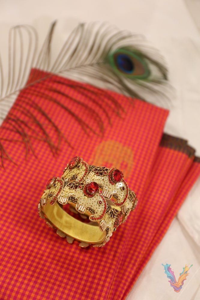 A red silk saree with gold motifs, styled with a golden embellished bangle