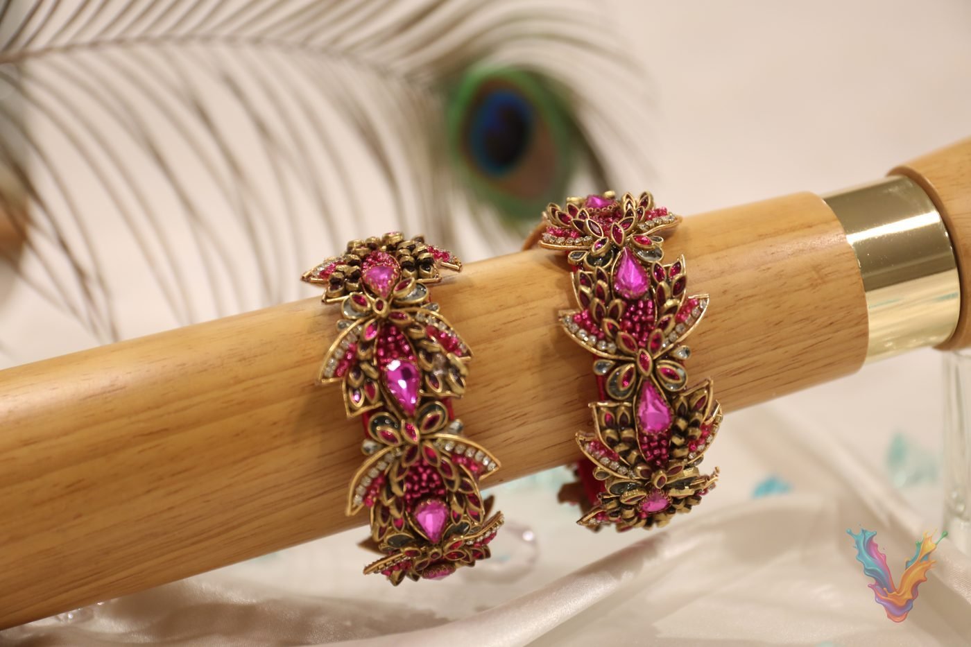 Red and gold beaded bangles on a wooden stand with a peacock feather