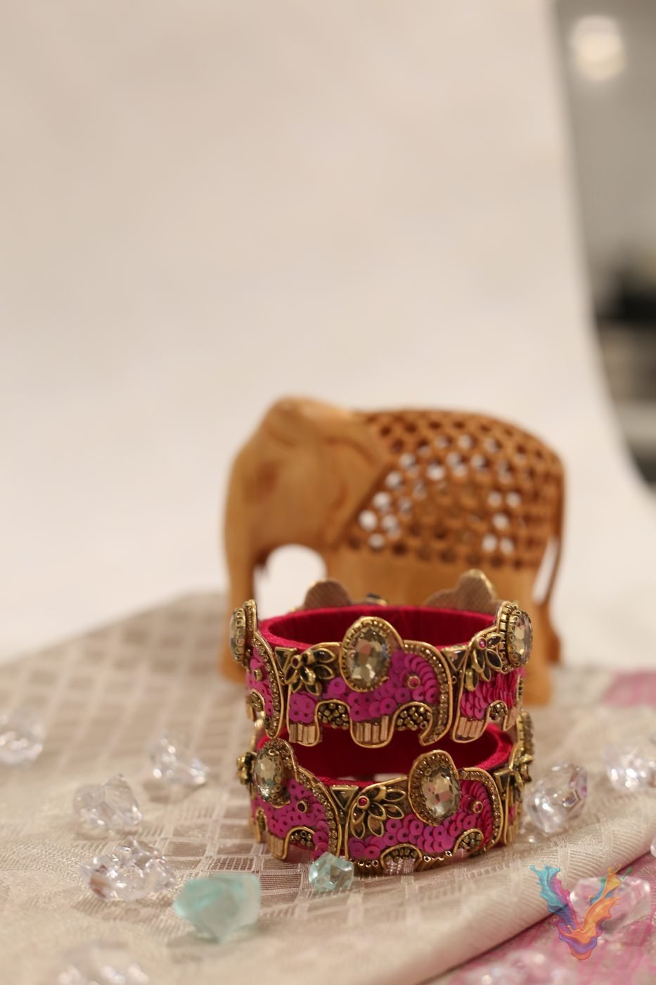 Thin gold and stone bangles arranged in color sets on a dark wooden stand