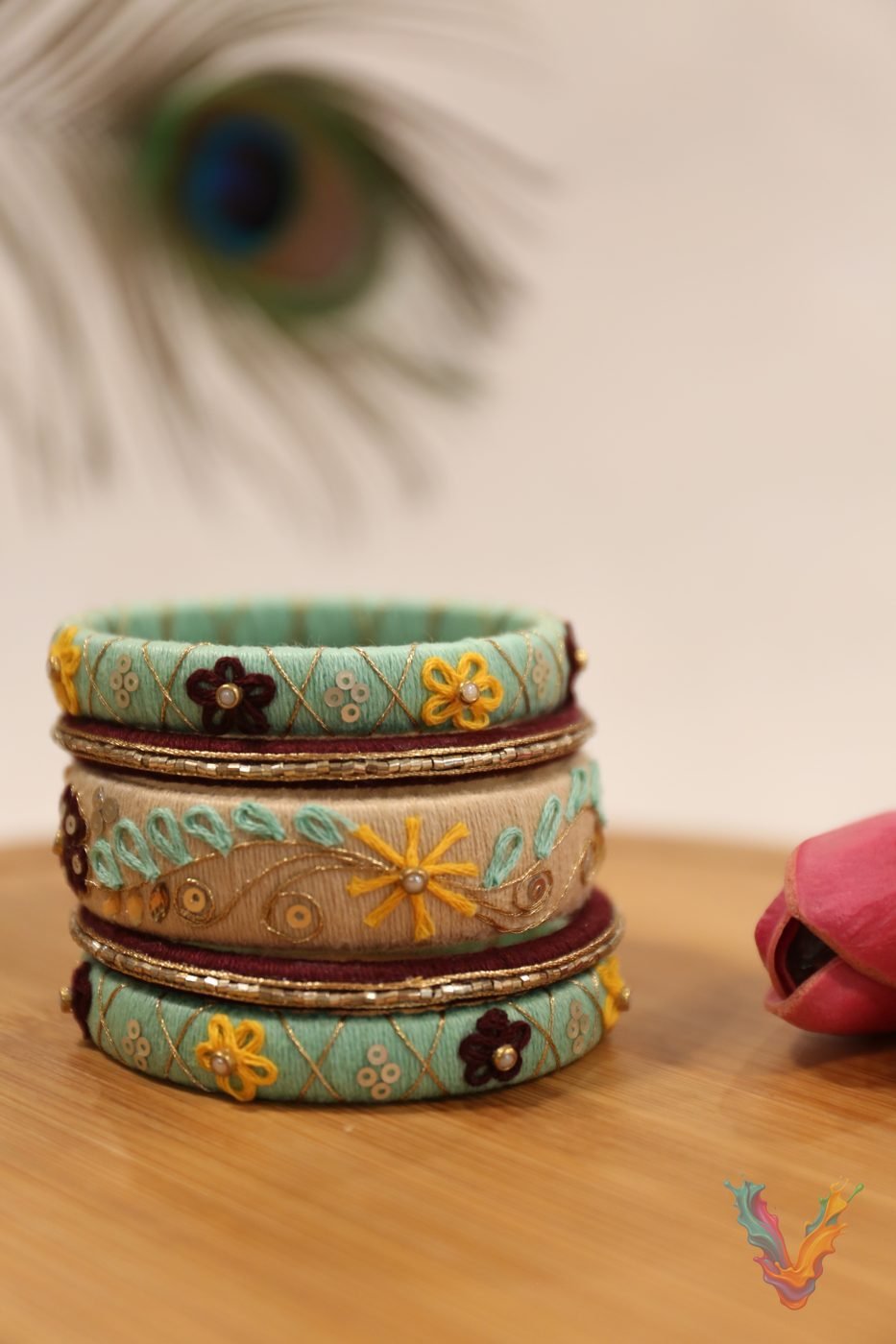 Turquoise silk thread bangles with gold floral details on a wooden table