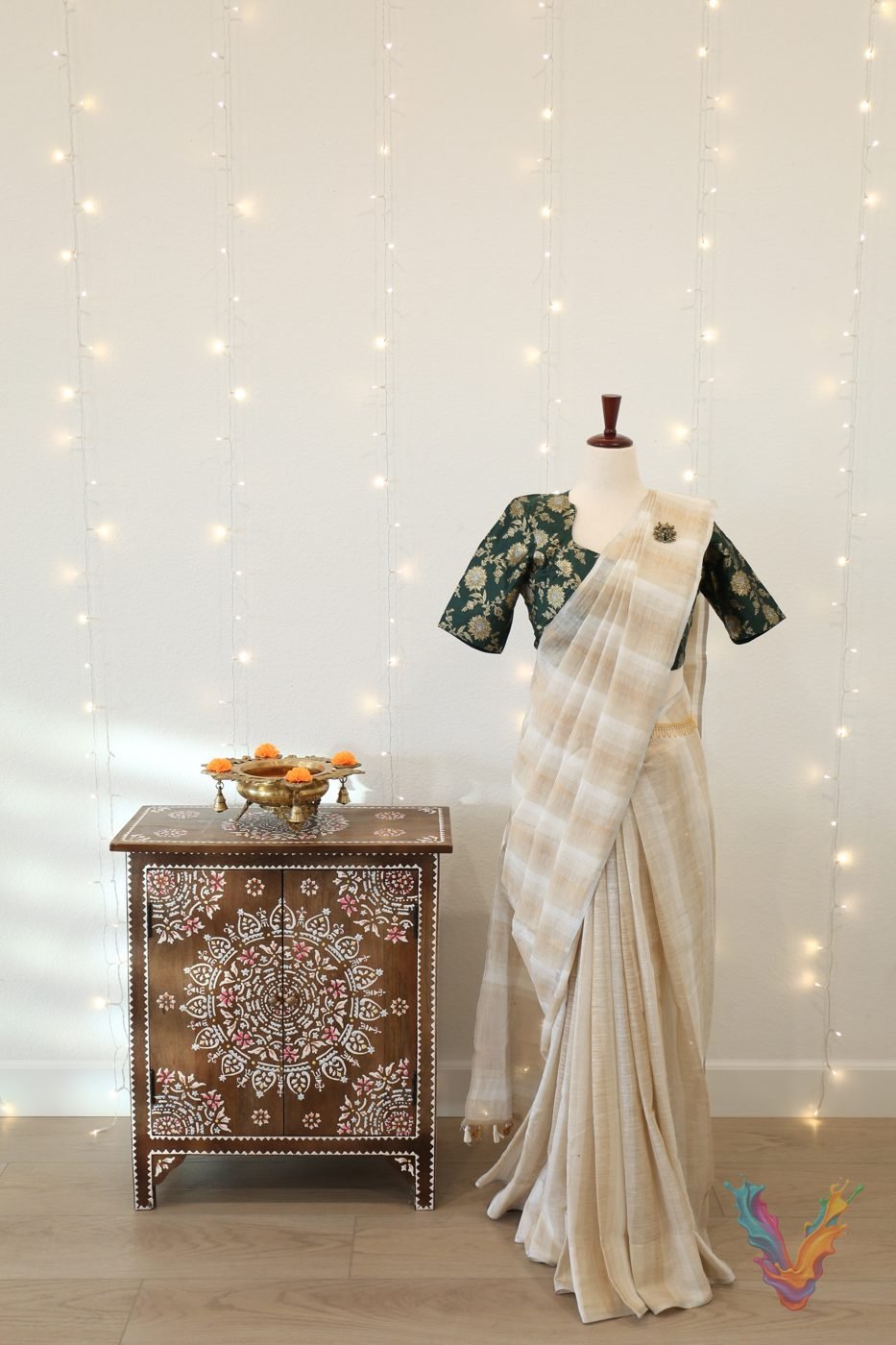 Ivory silk saree with green brocade blouse on a mannequin beside a painted chest